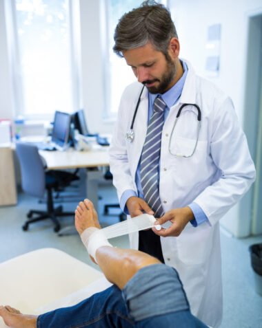 Male doctor bandaging foot of female patient in hospital