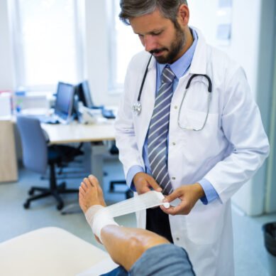 Male doctor bandaging foot of female patient in hospital
